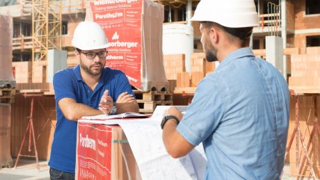 Two men with white helmets talking at a building site