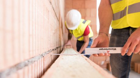 Two workers work on a brick wall