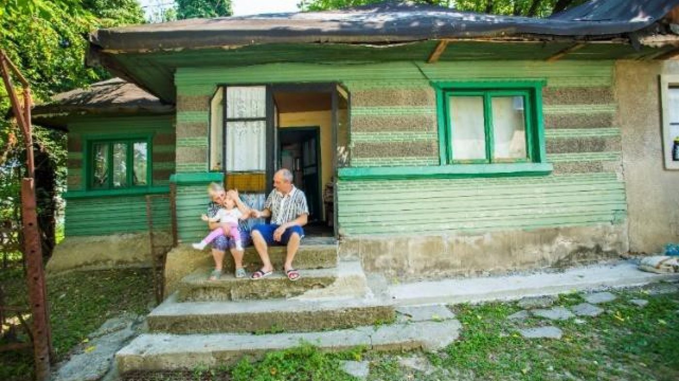 Eine Familie sitzt vor ihrem Haus, grüne Fenster