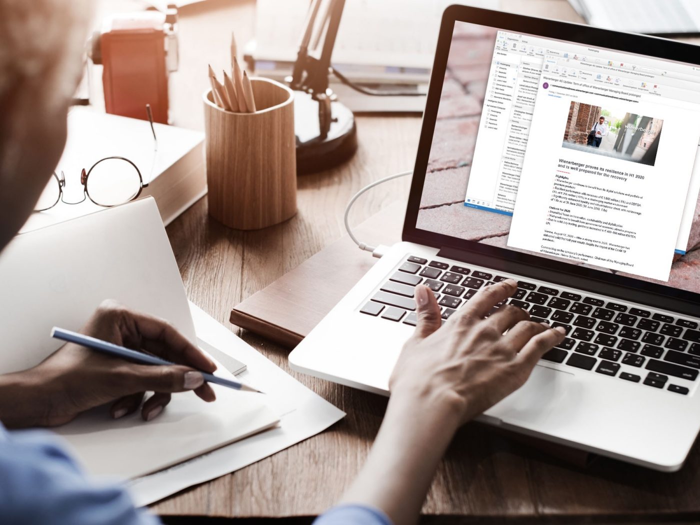 Frau tippt auf Laptop und schreibt dabei in ein Notizbuch