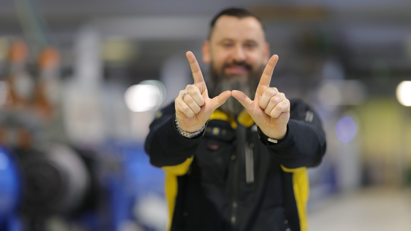Mitarbeiter in einer Produktionshalle formt W mit seinen Händen