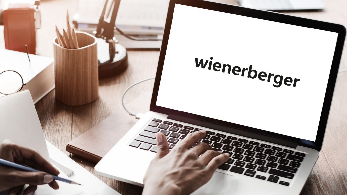 Jemand tippt auf einem Laptop, Bleistift und Block, Wienerberger Logo auf Bildschirm