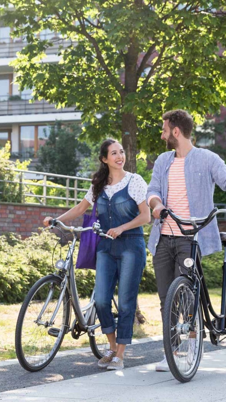 Frau und Mann schieben Fahrräder über gepflasterten Weg