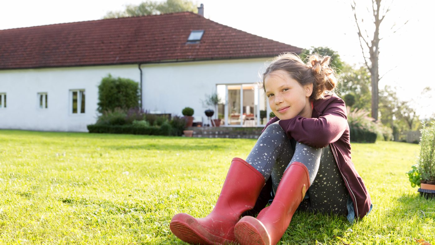 Mädchen sitzt auf einer grünen Wiese vor einem Haus
