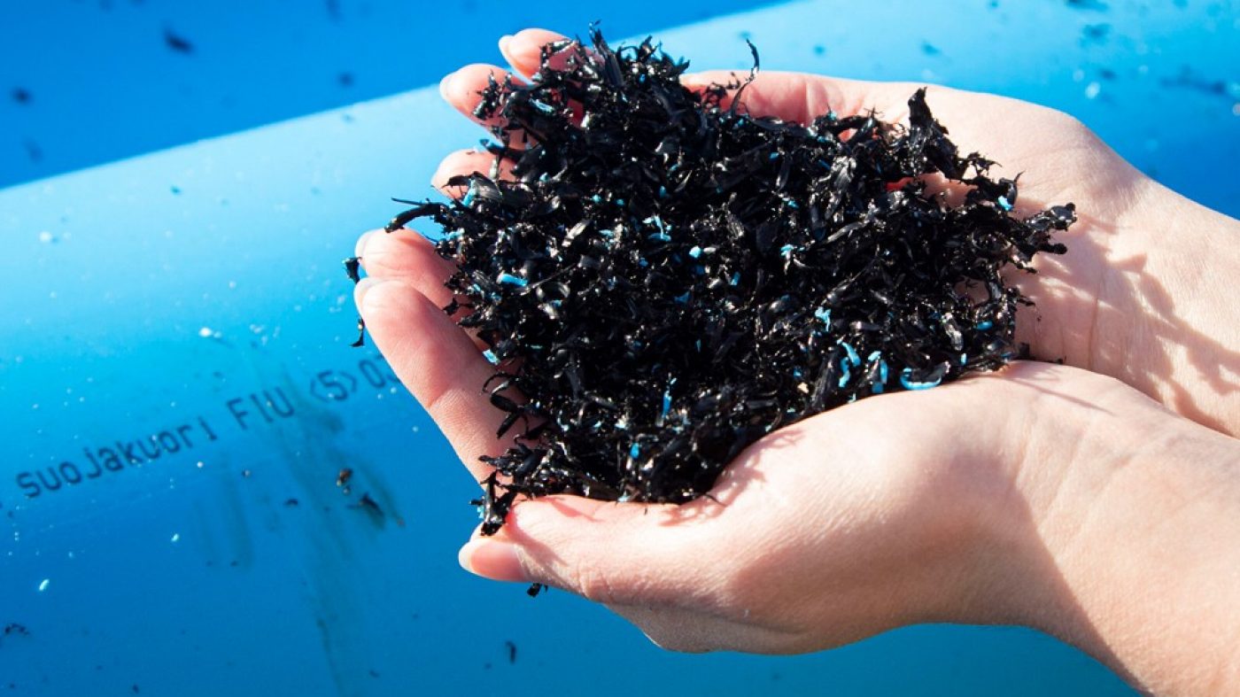 Hände halten recycelten Kunststoff für Pipelife Rohre, blaue Rohre im Hintergrund