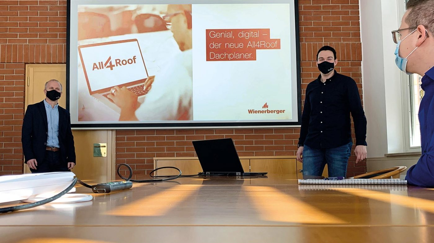 Zwei Männer stehen vor Leinwand, Beamer, Laptop, Masken