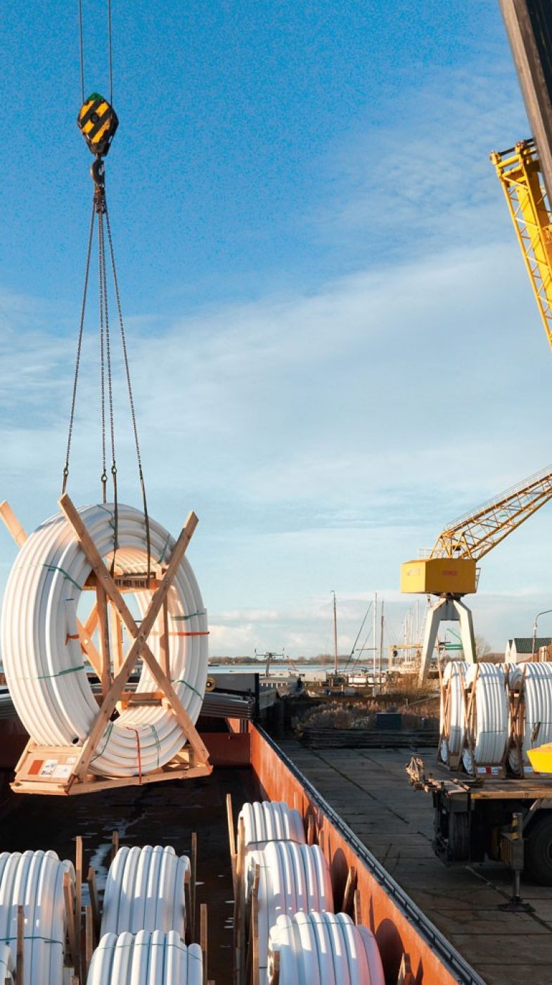 gelber Kran hebt Rohre von einem Schiff, blauer Himmel, zwei Männer