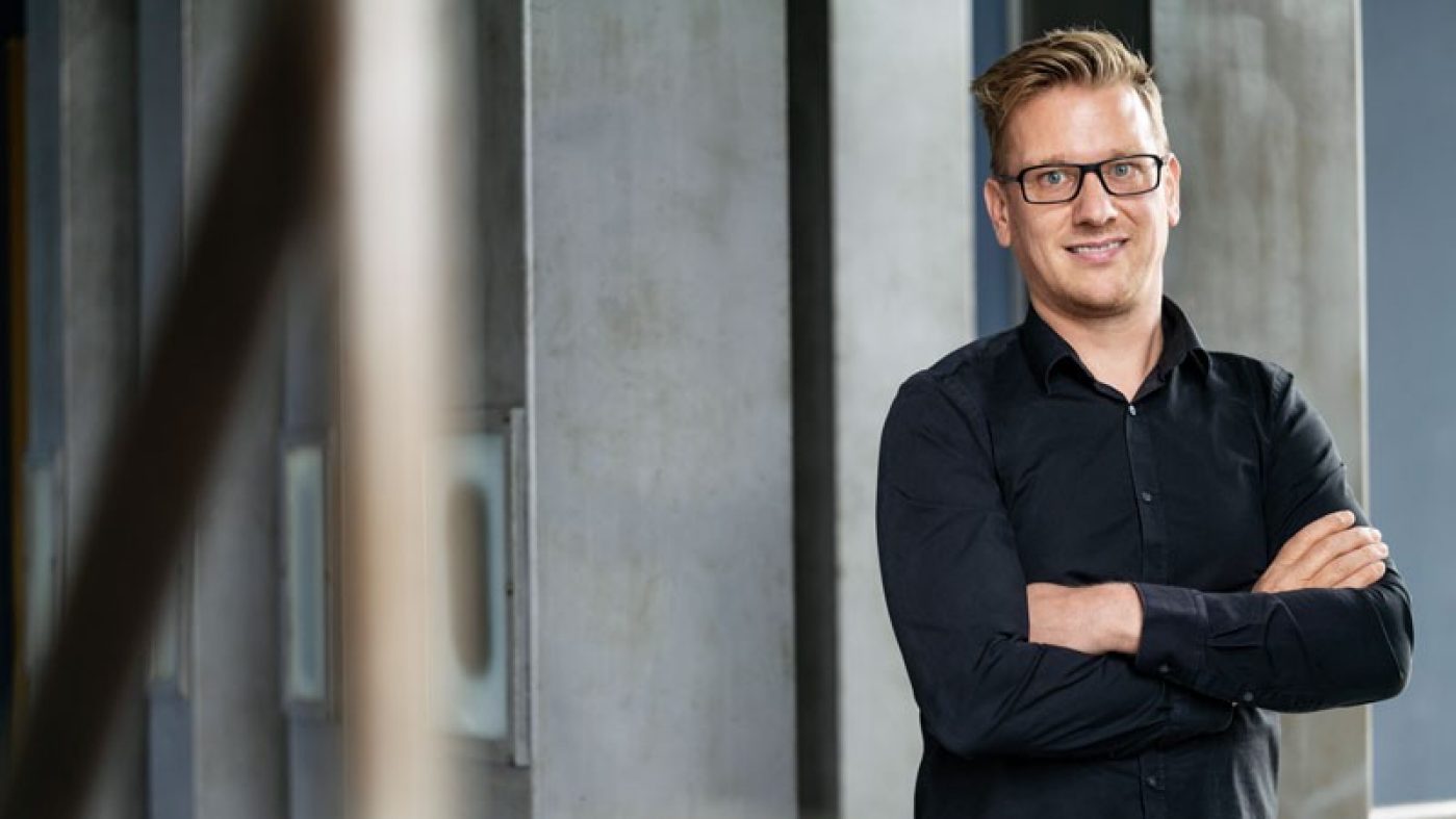 Gert Standaert steht mit verschränkten Armen vor grauen Säulen