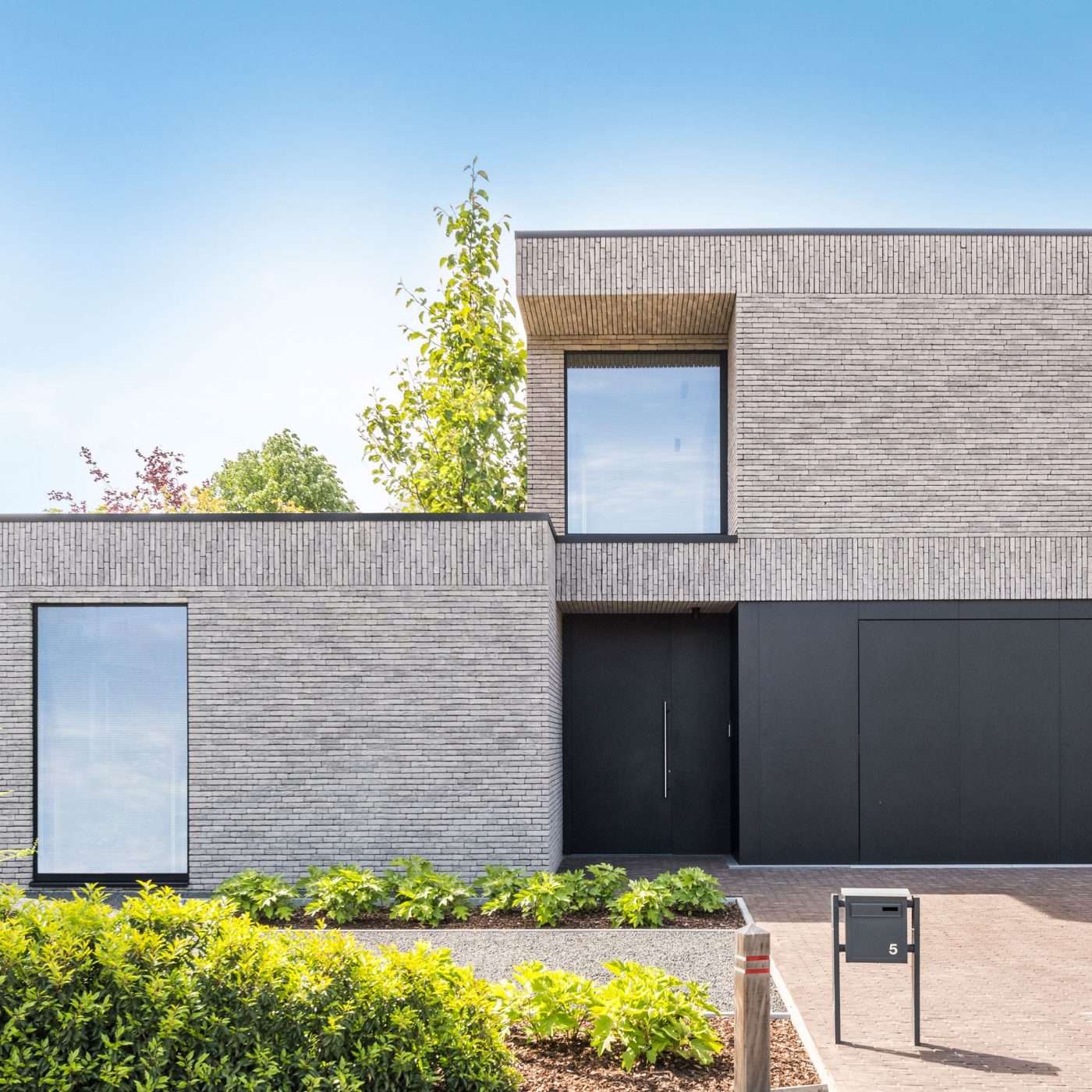 Haus mit Ziegelfassade, dunkelgraue Haustür, Bäume