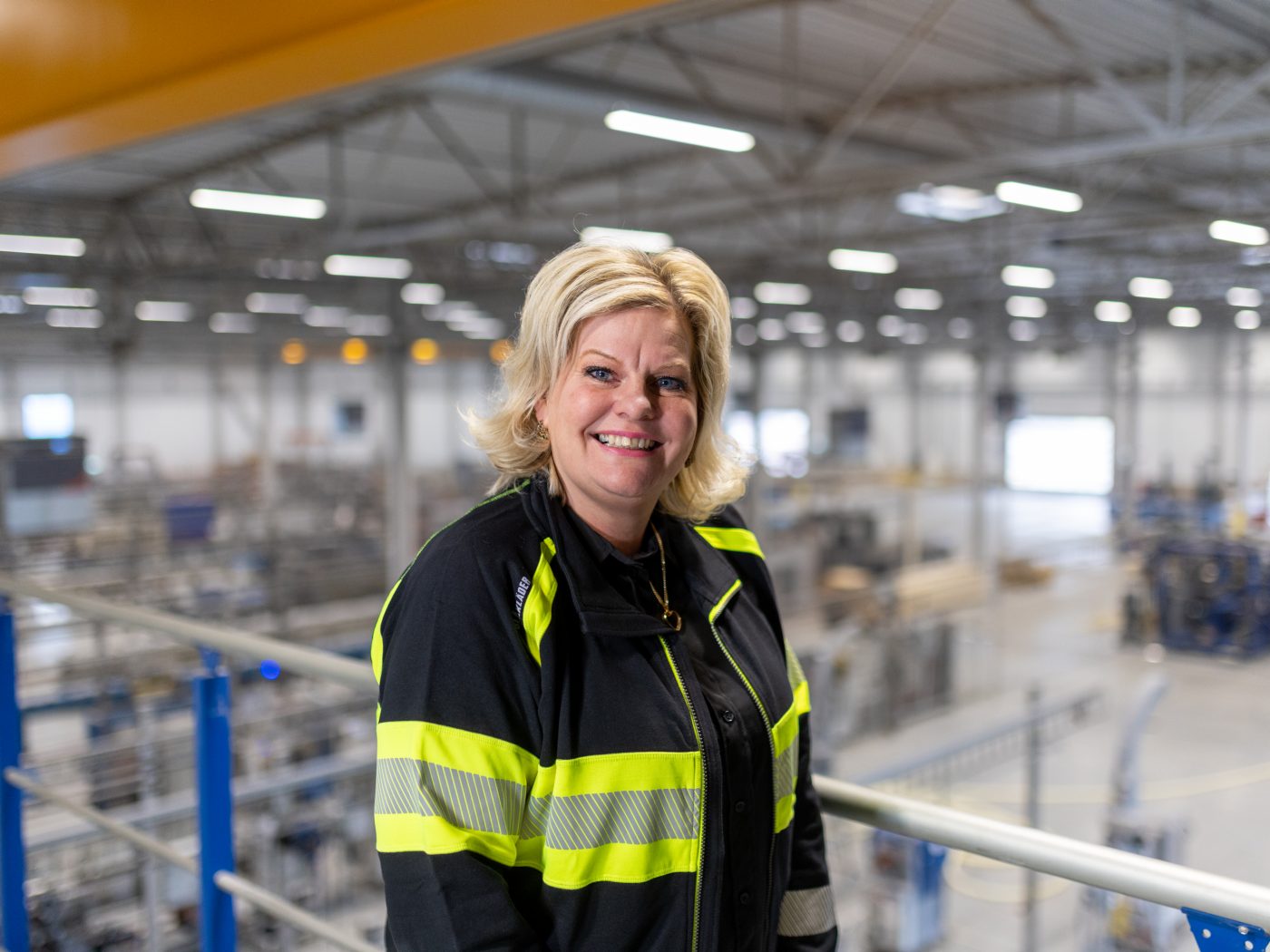 blonde Frau in einer Fabrik, lächelt in die Kamera