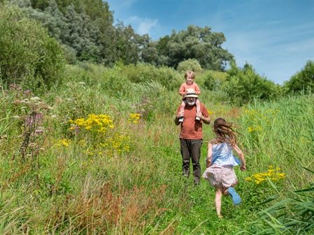 Girl running towards man with boy on shoulders, green landscape