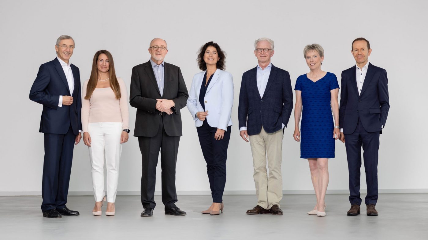 Sieben Personen stehen nebeneinander und schauen in die Kamera