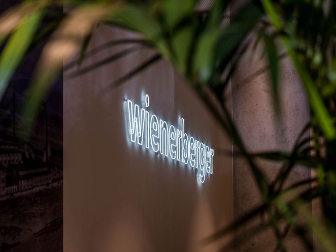 Wall with Wienerberger lettering from fluorescent tubes, green plant