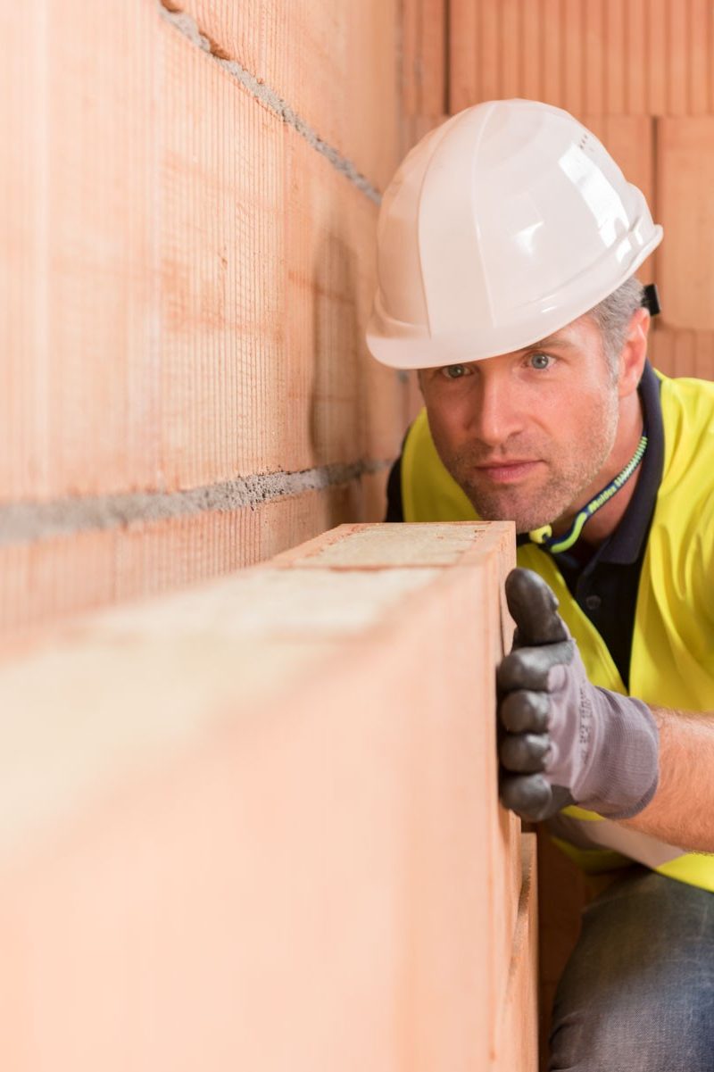 Construction worker checking alignment of mineral-wool filled clay block