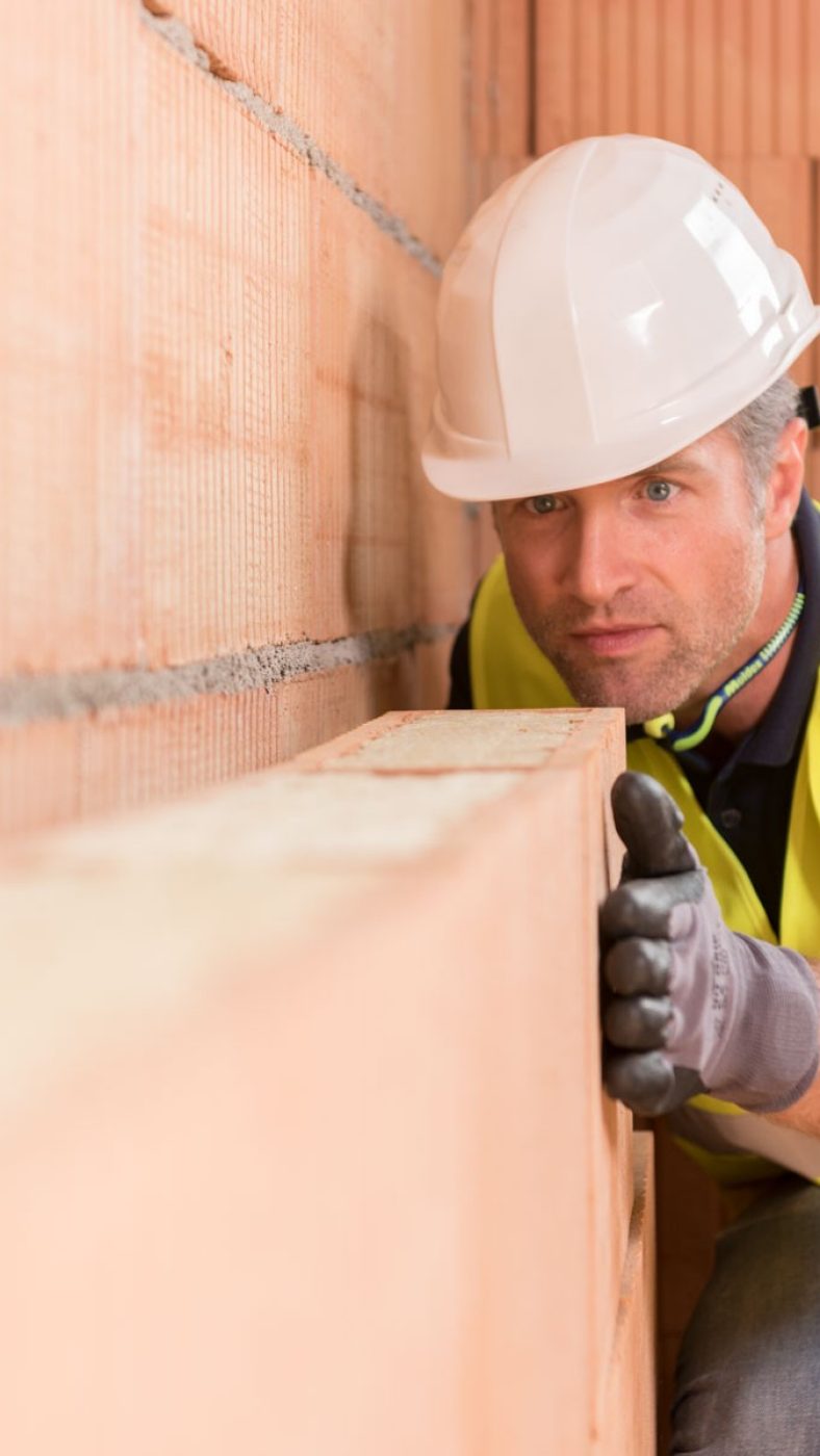 Construction worker checking alignment of mineral-wool filled clay block