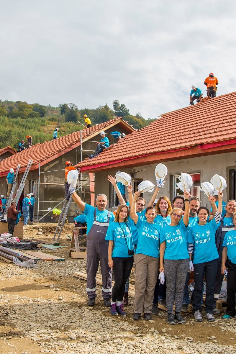 people in blue shirts holding white helmets in the air, houses being built