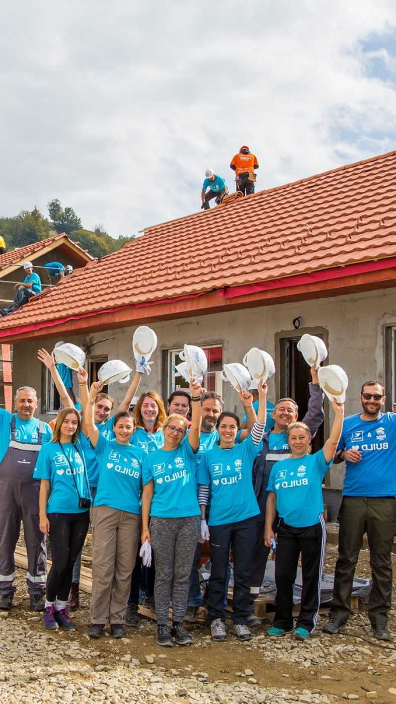 people in blue shirts holding white helmets in the air, houses being built