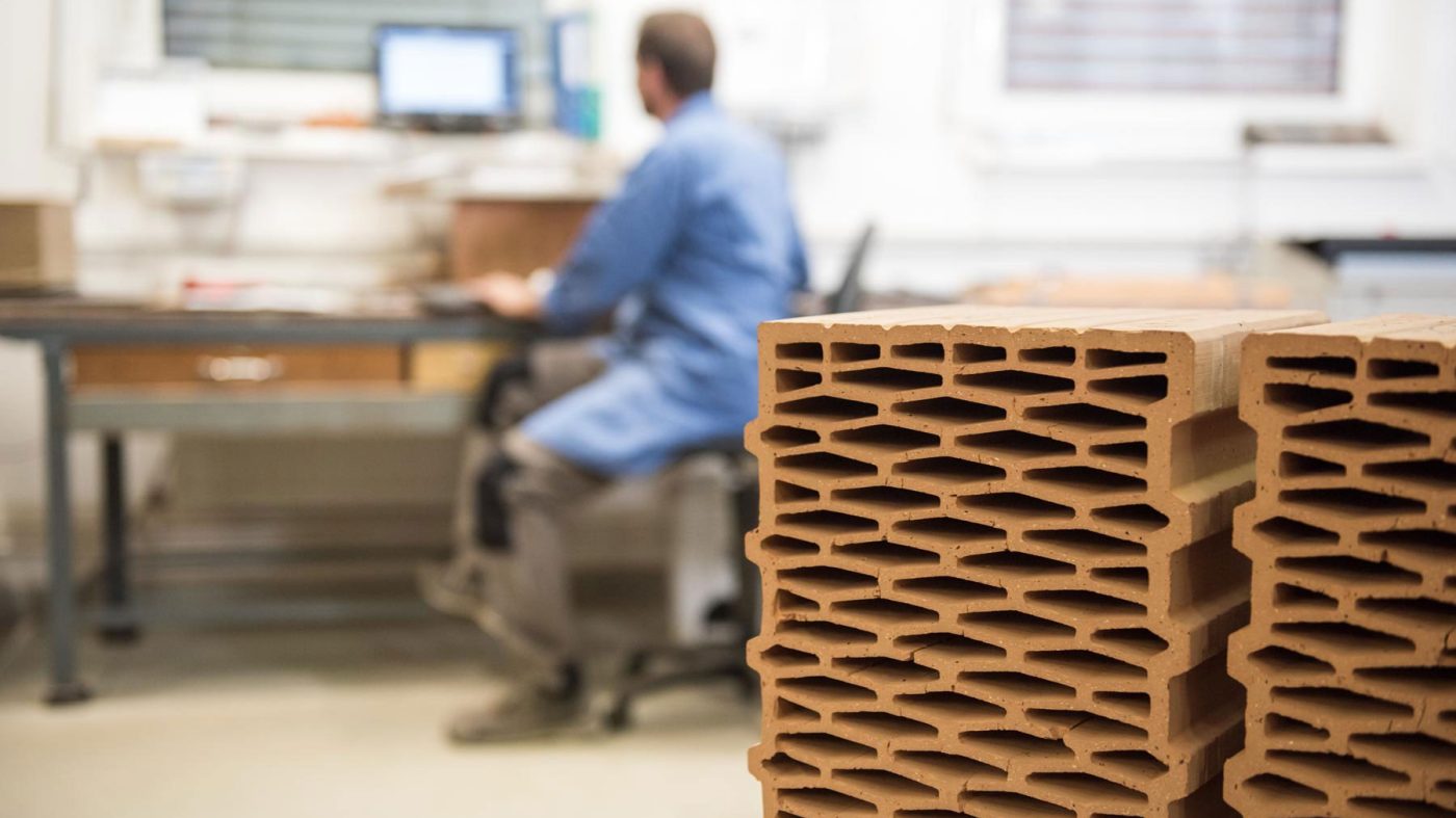Device with green display and buttons, man with white coat and safety goggles in background