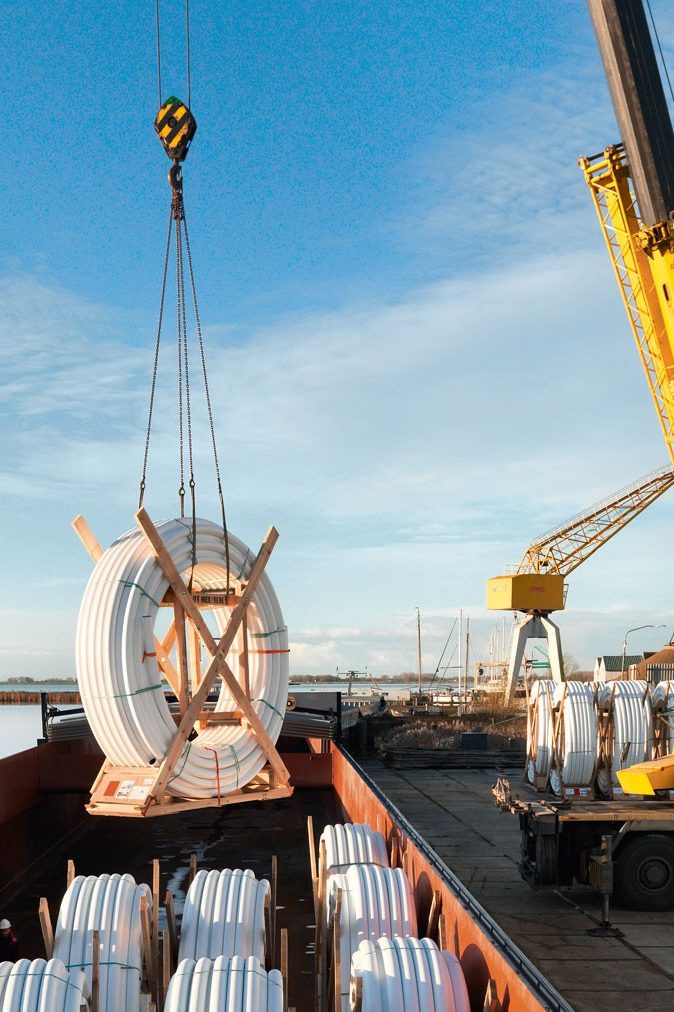 yellow crane lifts pipes from a ship, blue sky, two men