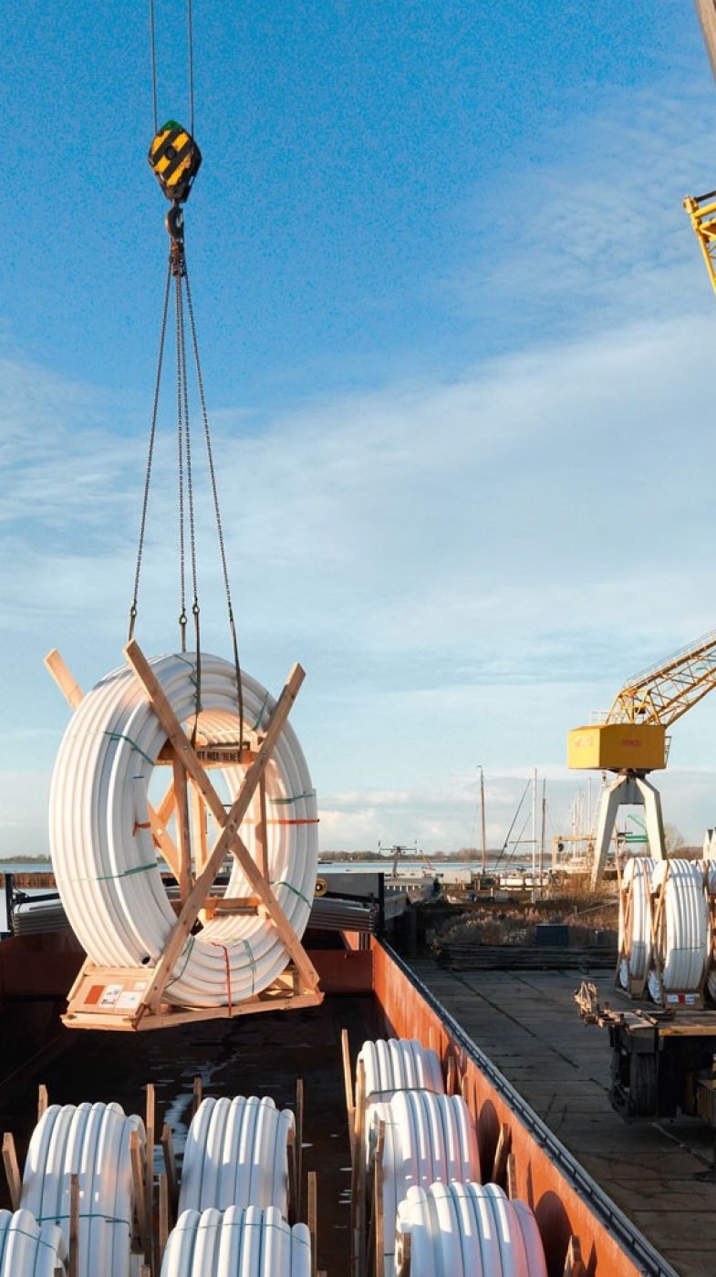 yellow crane lifts pipes from a ship, blue sky, two men