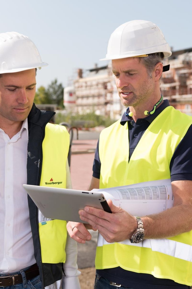 Two men with safety vest, helmet and a tablet