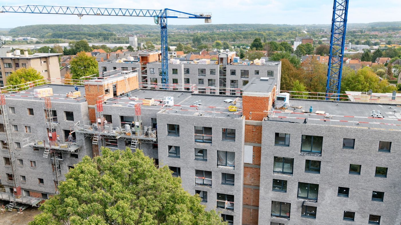 brick building under construction, trees, blue cranes