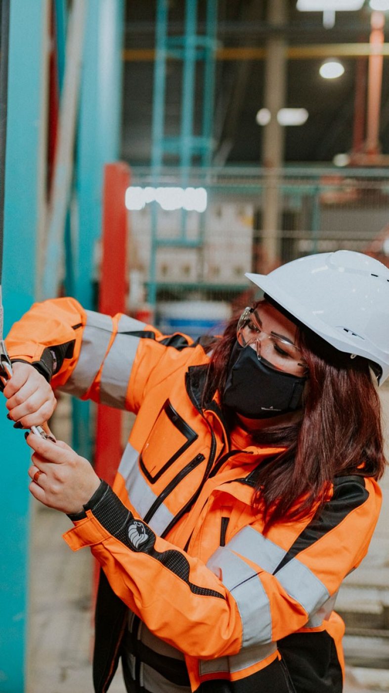 Woman helps man put on protective equipment, production hall from inside