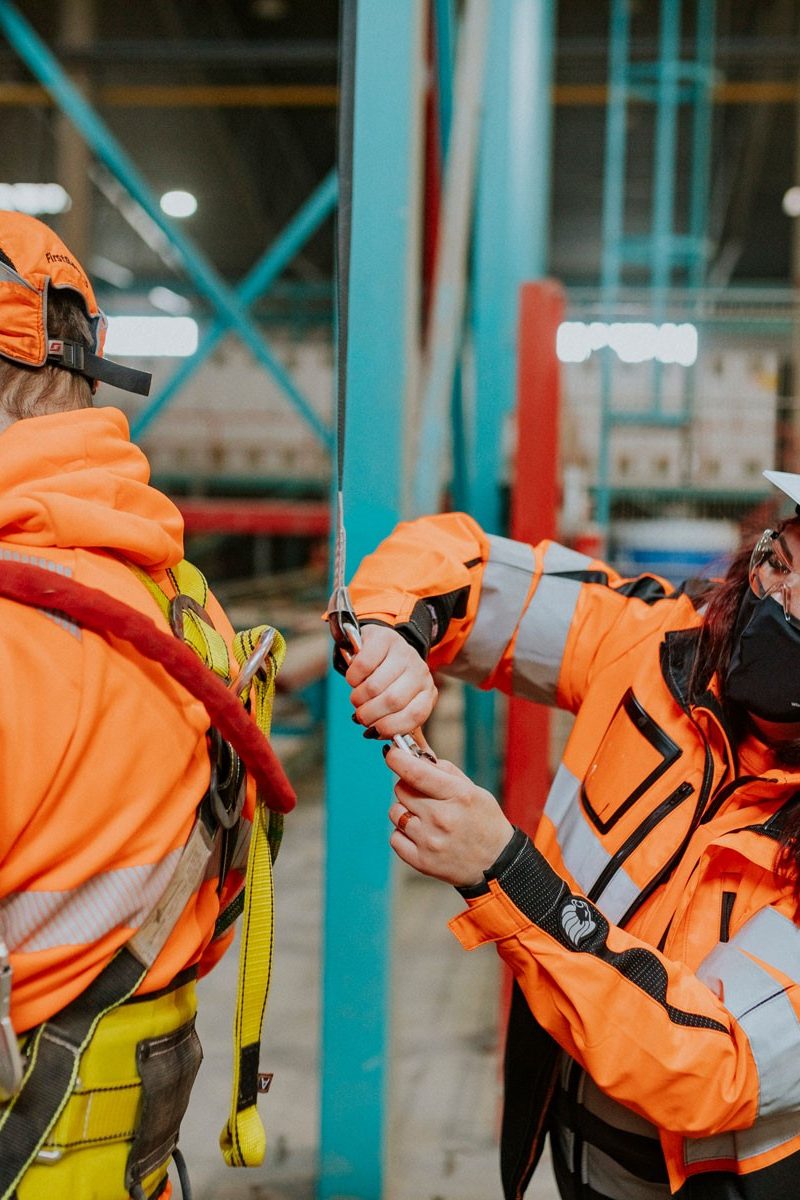 Woman helps man put on protective equipment, production hall from inside