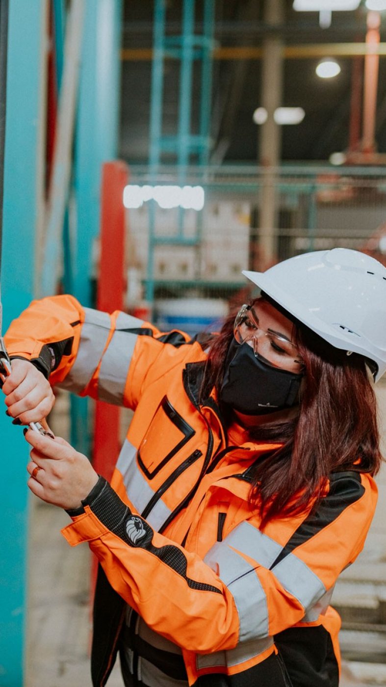 Woman helps man put on protective equipment, production hall from inside