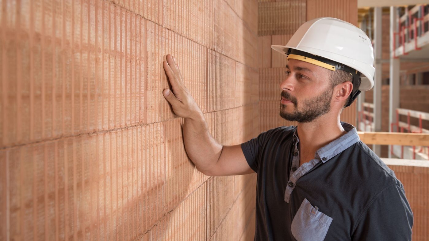 Man with white helmet touches brick wall