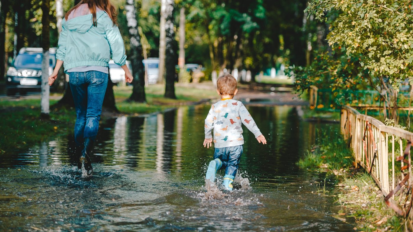 Woman child and child in rubber boots on flooded sidewalk