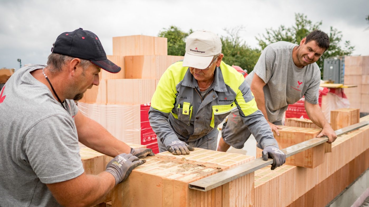 Three bricklayers in work clothes set bricks