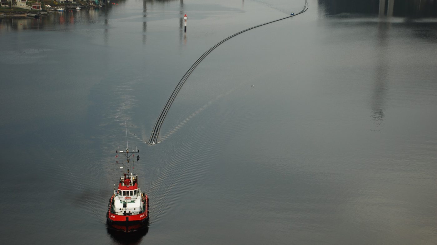 The boat tows long pipes through the water