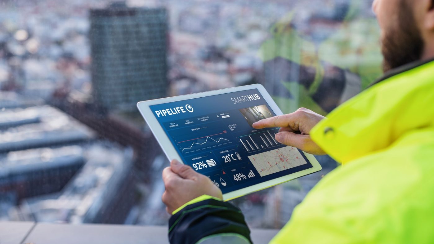Man with yellow safety jacket hold tablet with graphs and figures on it, city in the background