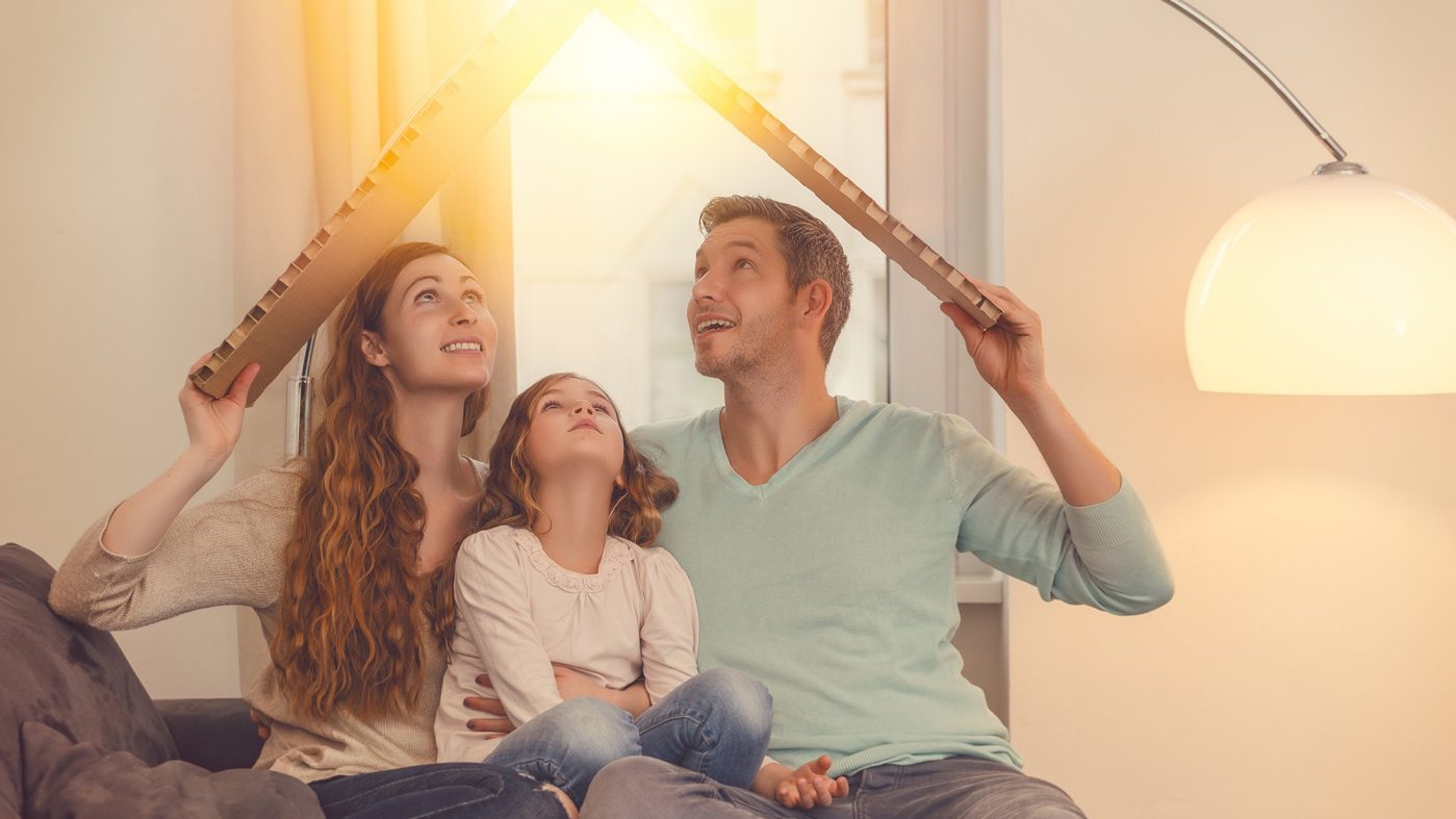 Woman, child and man on a couch, form a roof over their heads with cardboard, lamp