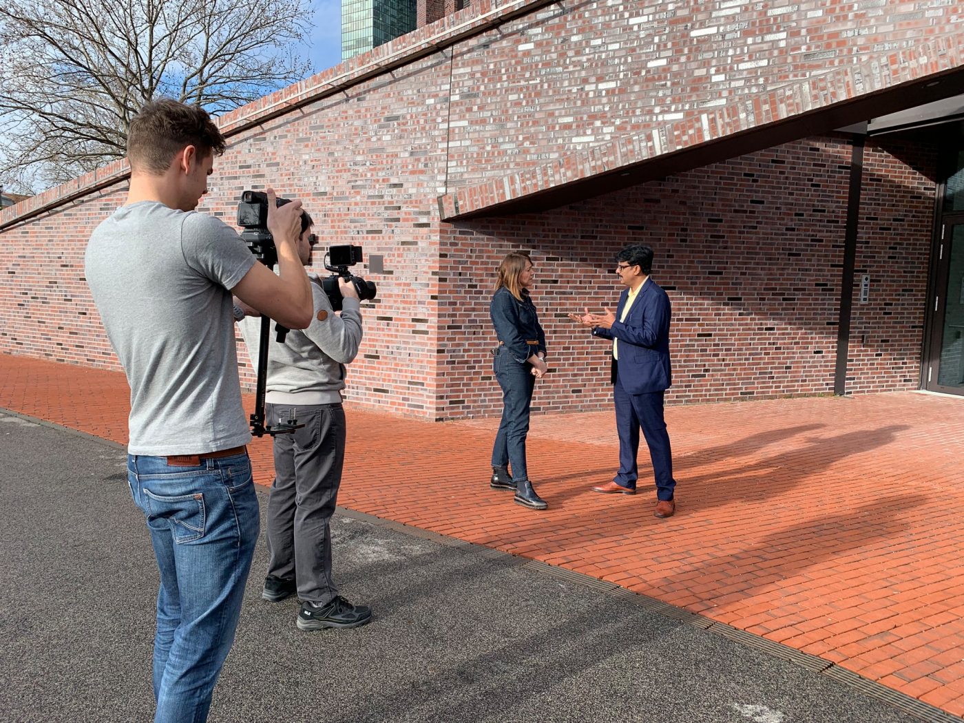 Interview scene in front of brick building, two camera men