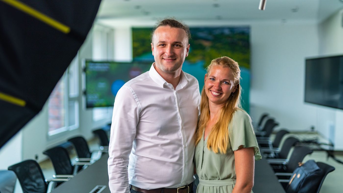 two people in a meeting room standing together and smiling into the camera