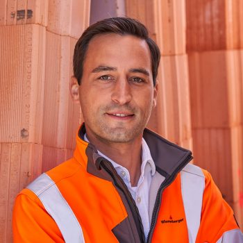 Man wit h savety jacket in front of clay bricks, looks into camera