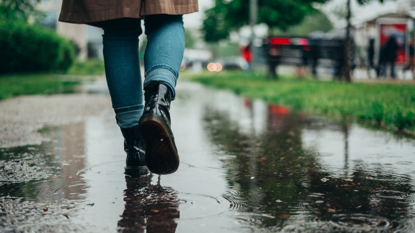 Woman legs walking on puddles while it rains in the city