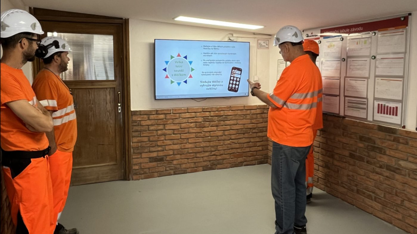Employees stand in a meeting room and look at a screen