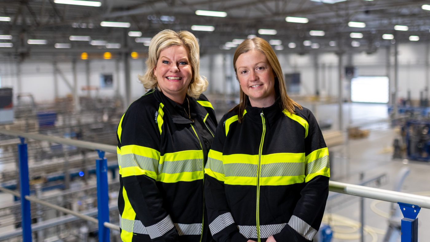 Two women in a factory, smiling into the camera