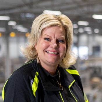Blond woman in a factory building smiling into the camera