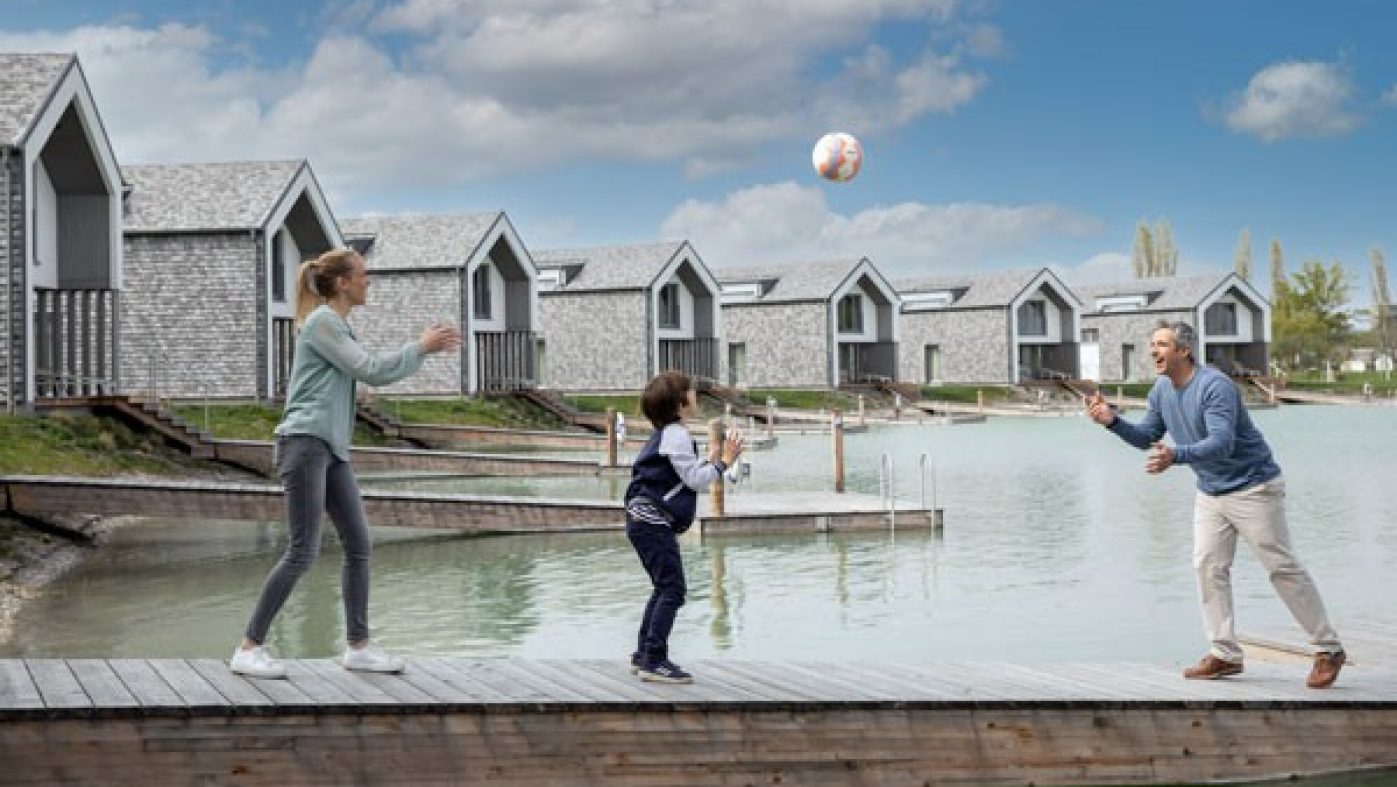 Family playing with ball on pier, houses in background