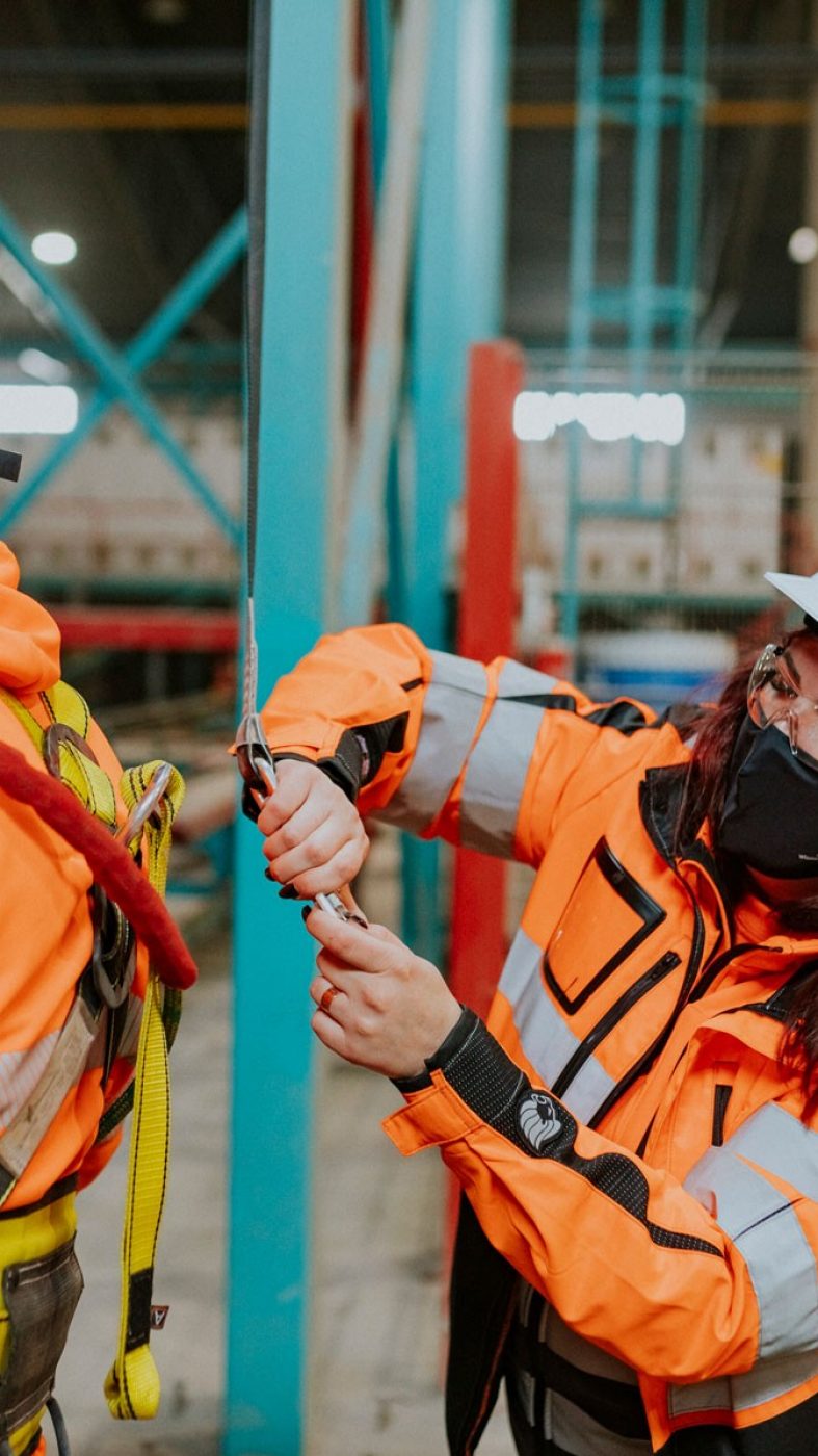 A woman in safety gear attaching a safety line to a coworker
