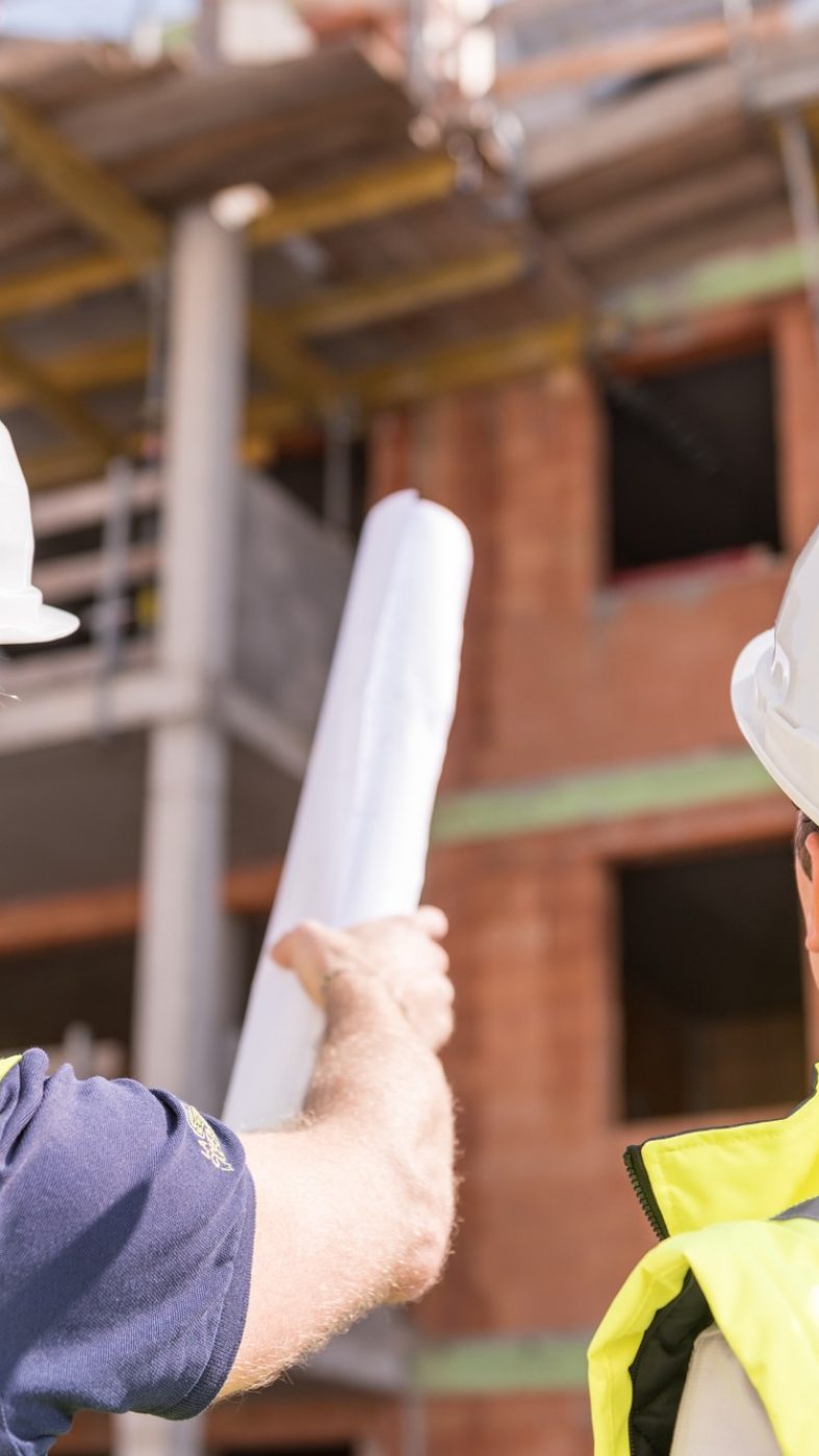 two men with safety clothes and white helmets on a building site, looking at the building